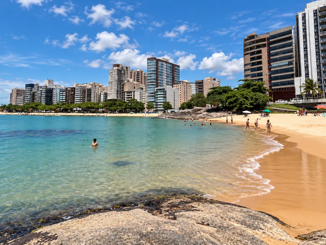 Praia dos Namorados, em Guarapari, com águas calmas, pedras e prédios ao fundo